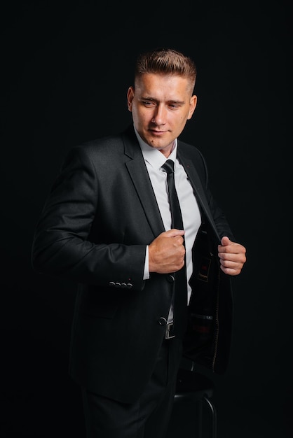 A handsome young man wears a stylish black suit and smiles on a black background. Clean up, prepare.