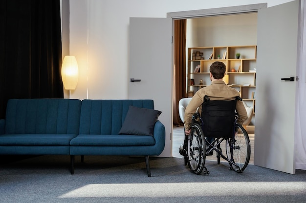 Photo a handsome young man in a wheelchair moves around the apartment getting used to a new life recovery after injury or ill lonely at home