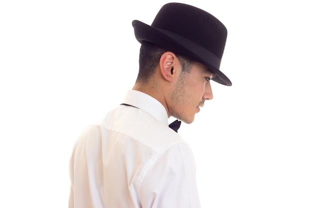 Handsome young man in white shirt with black bowtie and black hat on white background in studio