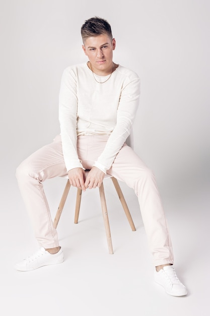 白いセーターとズボンのハンサムな若い男は椅子に座っています