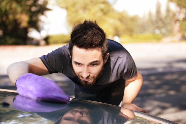 Handsome young man wiping car with special glove