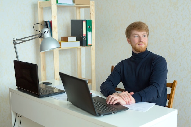 Фото Красивый молодой человек с рыжей бородой работает в своем офисе за ноутбуком
