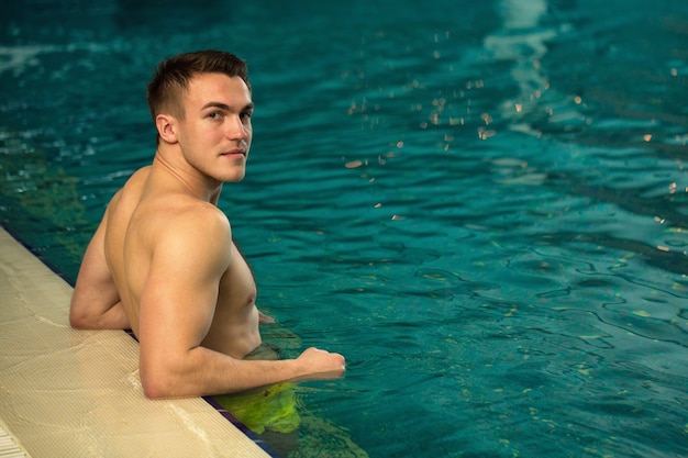 Handsome young man with athletic toned body resting by the swimming pool