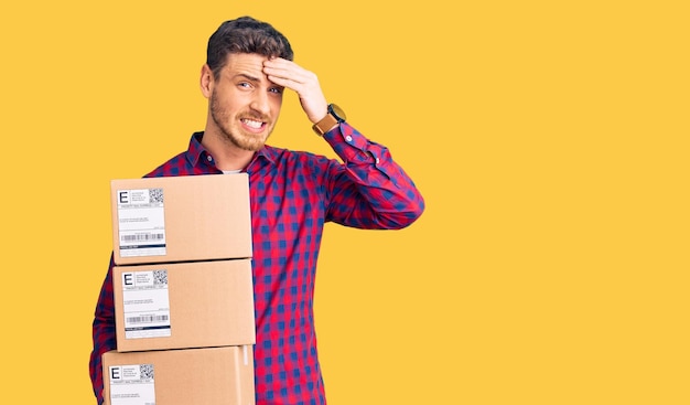 Handsome young man with bear holding delivery packages stressed and frustrated with hand on head surprised and angry face