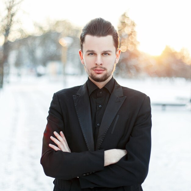 Handsome young man with a beard wearing a black suit on a sunset