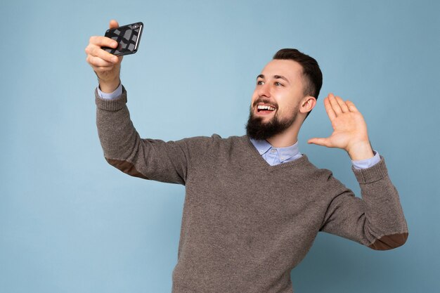 カジュアルな灰色のセーターを着ているひげを持つハンサムな若い男