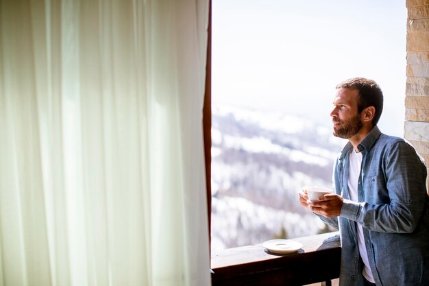 Handsome young man with cup of hot tea at the winter window