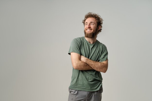 Handsome young man with curly hair in olive t-shirt looking at front isolated on white wall