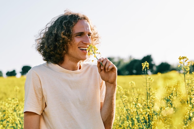 handsome young man with curly hair with a flower in a rapeseed flower field in spring