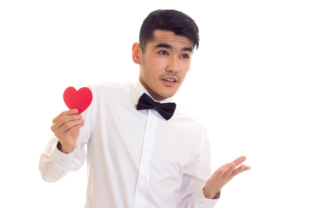 Handsome young man with dark hair in white Tshirt with black bowtie holding a red paper heart