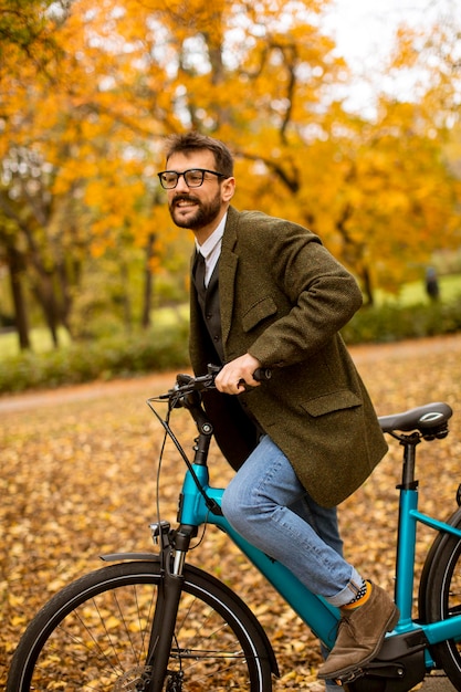 Bel giovane con bicicletta elettrica nel parco autunnale