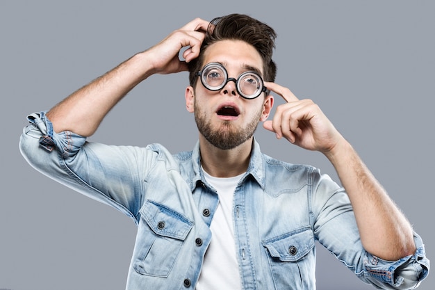 Photo handsome young man with funny glasses joking and making funny face over gray background.