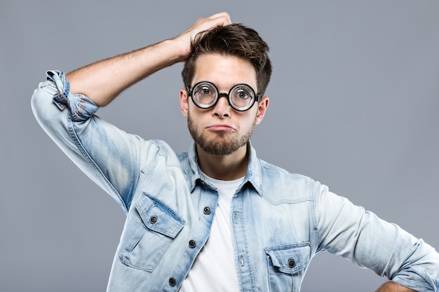 Handsome young man with funny glasses joking and making funny face over gray background.