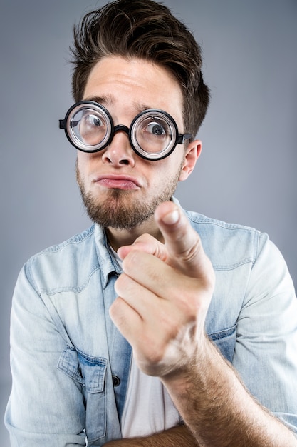 Handsome young man with funny glasses joking and making funny face over gray background.