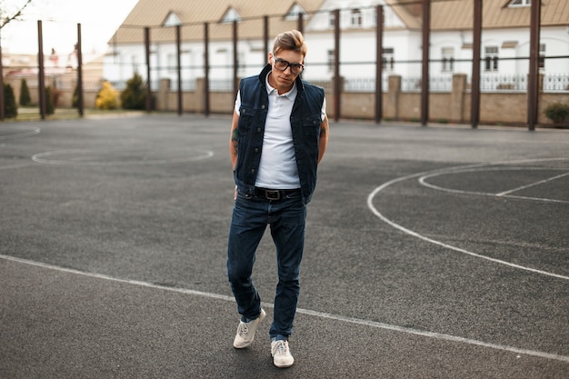Фото Красивый молодой человек в очках в винтажном стиле джинсов гуляет по улице