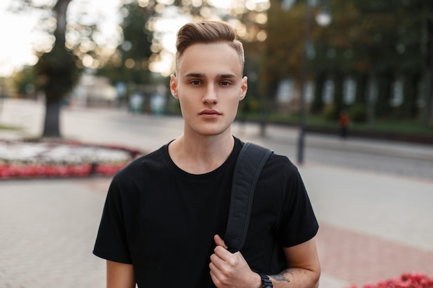 Handsome young man with a haircut with a backpack on the of the city