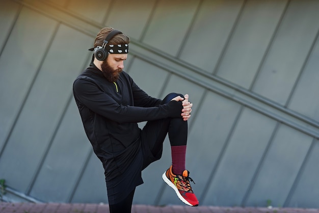 Handsome young man with headphones doing stretching and warmup exercises before running while