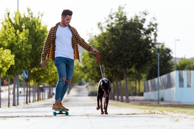 公園でスケートボードをしている彼の犬のハンサムな若い男。