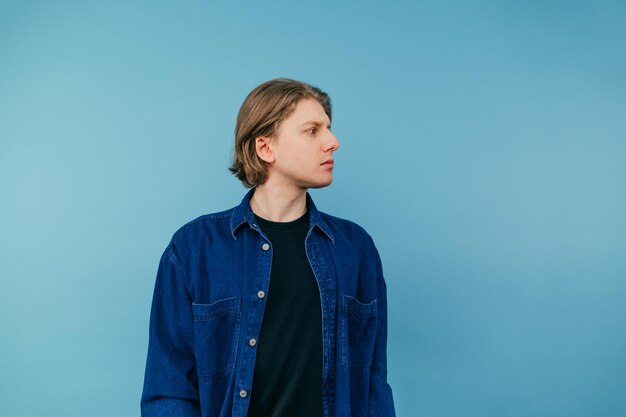 Handsome young man with long hair in casual clothes stands on a blue background