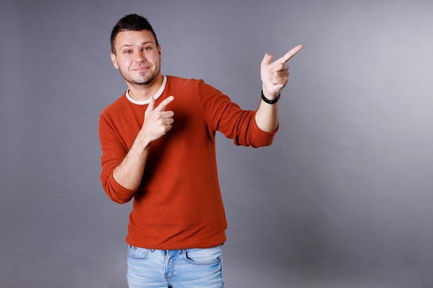 Handsome young man with an orange sweater pointing up