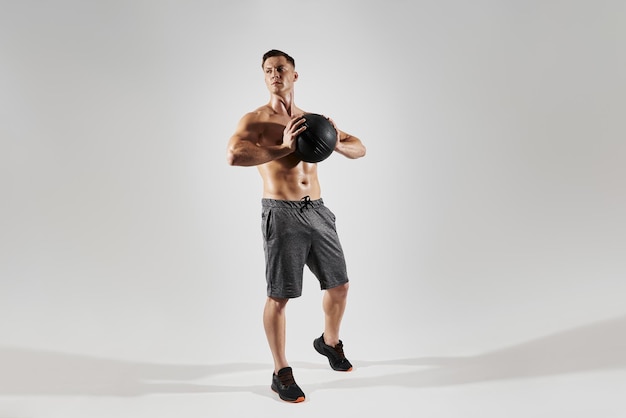 Photo handsome young man with perfect body holding medicine ball against white background