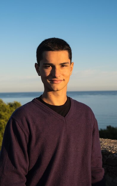 Handsome young man with positive attitude posing for camera with sea in background