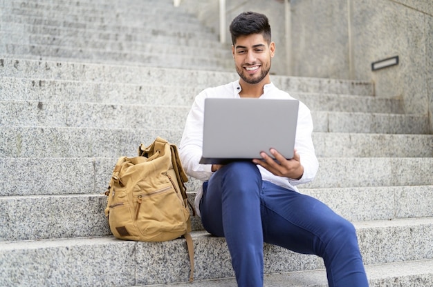 Handsome young man working with laptop on stairs