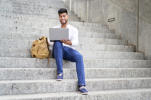 Handsome young man working with laptop on stairs