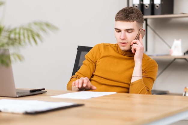 Handsome young man works with documents in the office and solves problems by phone