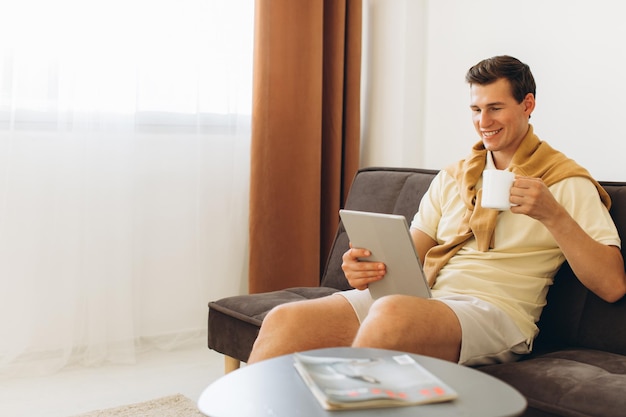 Handsome young man in yellow casual clothes sitting at home reading books and drinking coffee