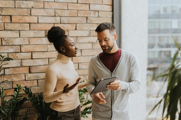 Photo handsome young multiethnic business couple with digital tablet standing and discussing in the modern office