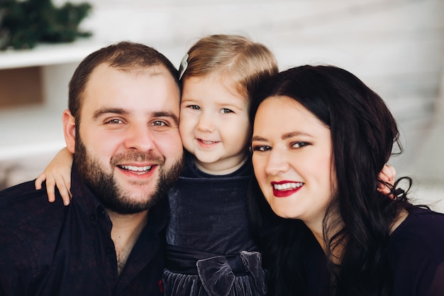 Handsome young mum with long black wavy hair, attractive strong dad with short dark hair spend Christmas time together with their little daughter