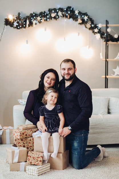 Handsome young mum with long black wavy hair, attractive strong dad with short dark hair spend Christmas time together with their little daughter