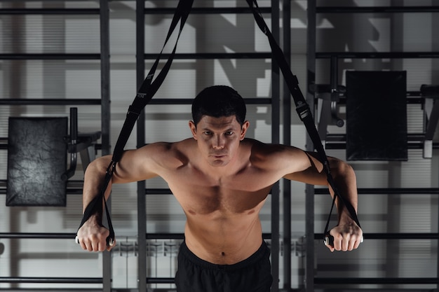 사진 체육관에서 운동하는 동안 잘생긴 젊은 근육질의 남자가 trx로 훈련합니다.