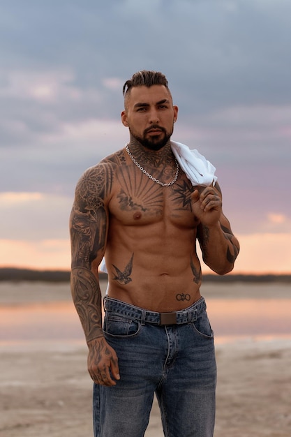 Foto bel giovane uomo italiano muscolare in posa senza camicia sulla spiaggia al tramonto ora legale
