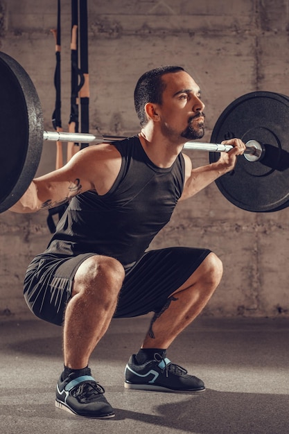 Photo handsome young muscular man doing squat exercise with barbell at the gym.