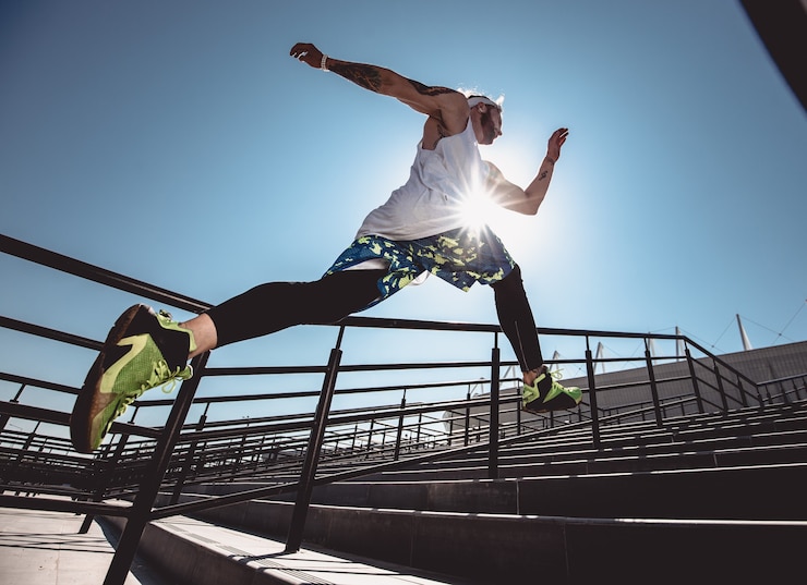 Photo handsome young muscular man in modern sport clothing run up the stairs outdoor at bright sunny day. wide angle photo of a jogging man. sport lifestyle .