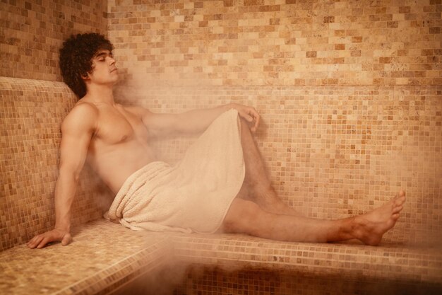 Handsome young muscular man relaxing and enjoying in the steam bathroom at the spa centre.