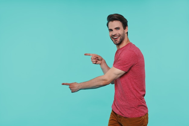 Bel giovane uomo sorridente in abbigliamento casual che guarda la macchina fotografica e punta lontano