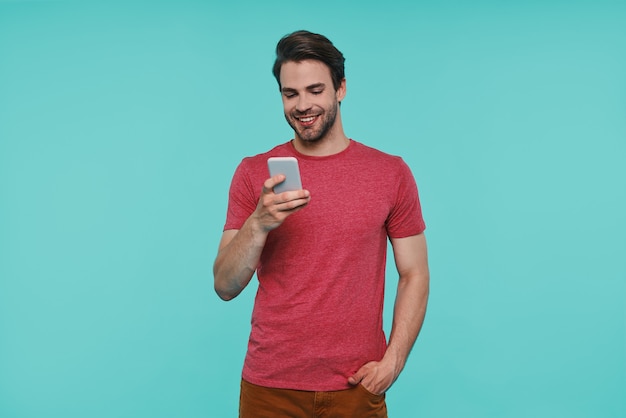 Handsome young smiling man in casual clothing texting on smart phone