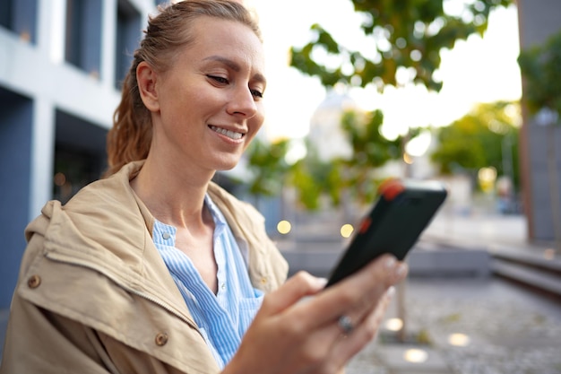 通りを歩いて携帯電話でハンサムな若い笑顔の女性