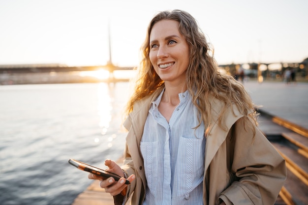 Handsome young smiling woman with mobile phone walking on the street