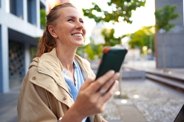 通りを歩いて携帯電話でハンサムな若い笑顔の女性