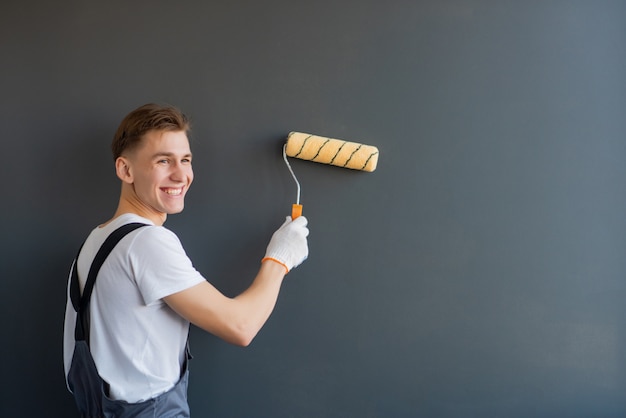 Giovane lavoratore sorridente bello con il rullo di pittura su fondo grigio