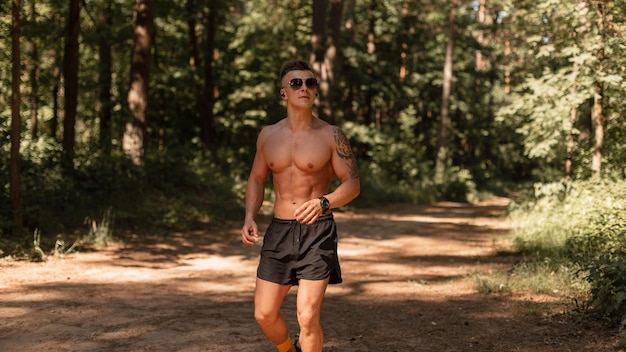 Handsome young sports athlete man runner with sunglasses and headphones runs through the forest and listens to music