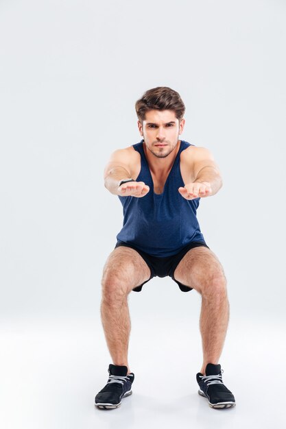 Photo handsome young sportsman doing squats over white background