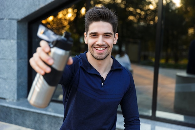 Handsome young sportsman drinking water from a bottle outdoors