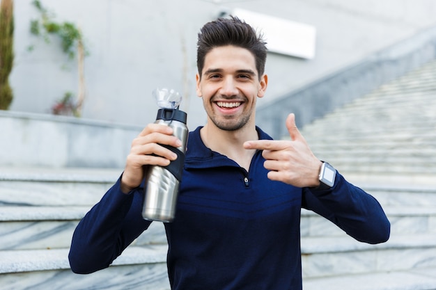 Handsome young sportsman drinking water from a bottle outdoors