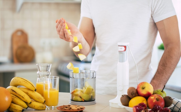 Bel giovane uomo sorridente sportivo in cucina sta preparando insalata di frutta vegana sana e frullato di buon umore