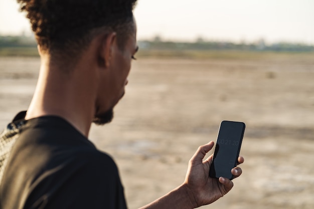 Bel giovane uomo sportivo forte utilizzando il telefono cellulare all'aperto